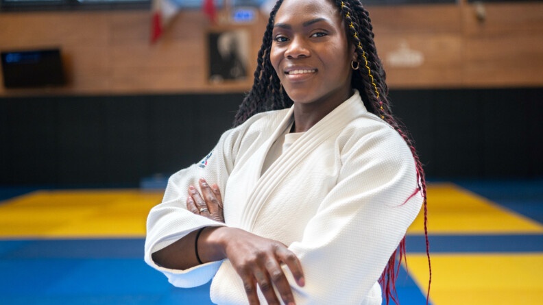 Portrait de la judokate Clarisse Agbégnénou en kimono devant des tatamis.