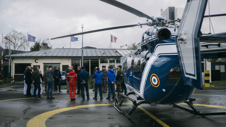 Hélicoptère bleu de la gendarmerie au premier plan, encore au sol, et au second plan briefing des pilotes avant l'exercice.