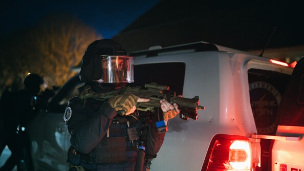 Un opérateur AGIGN de nuit avec UMP 45 devant le véhicule blindé