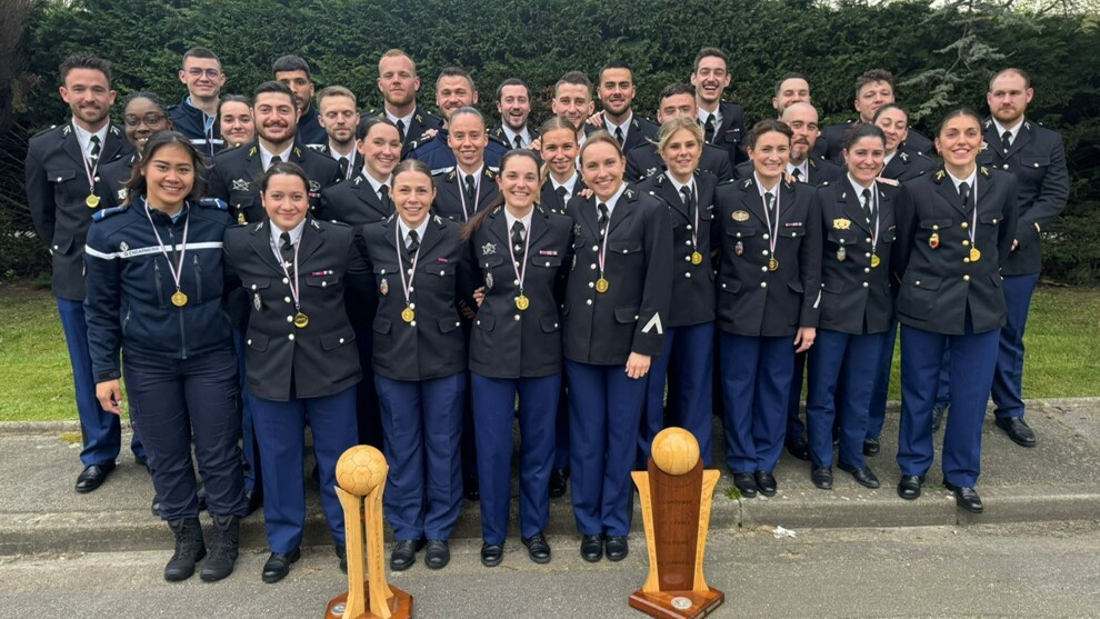 Groupe d'une trentaine de gendarmes et sportifs féminines et masculins de l'équipe de handball. Devant eux, deux grands trophées.