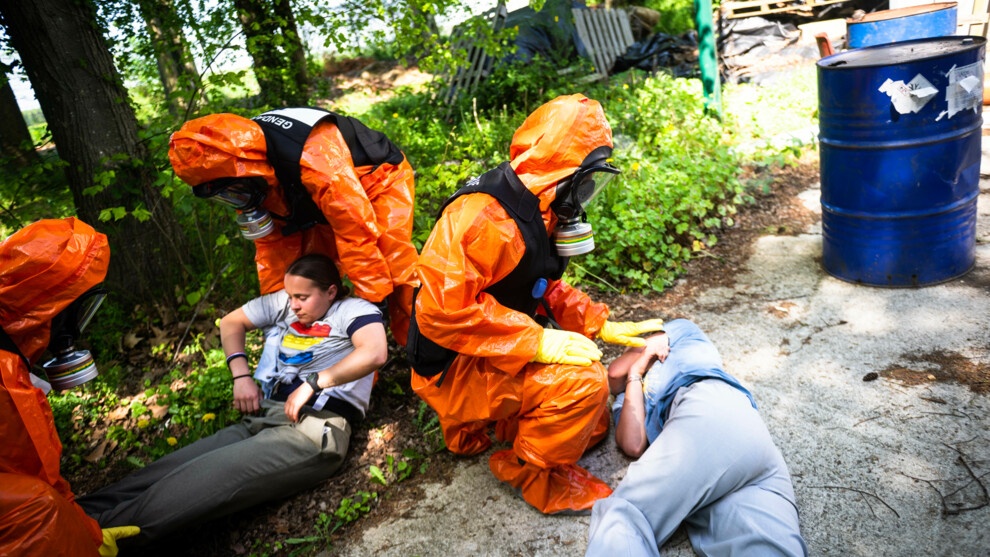 Trois gendarmes en combinaison NRBC portent secours à deux personnes allongées sur le sol.