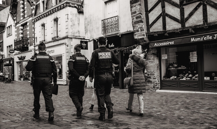 2 gendarmes et un policier de dos ainsi qu'une femme, marchant dans une rue pavée.
