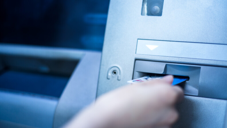 Une main entrain d'insérer une carte de crédit au guichet automatique d'une banque