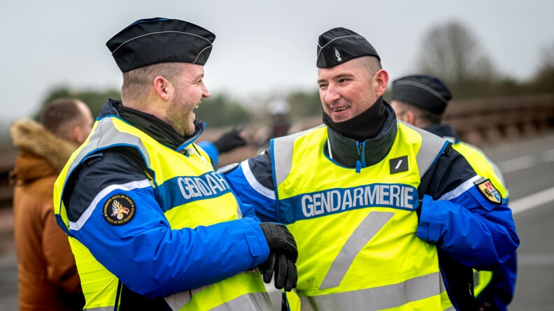 Photo de deux réservistes de la gestion des flux entrain de rigoler ensemble. Dans le fond on aperçoit un civil discuter avec d'autres gendarmes.