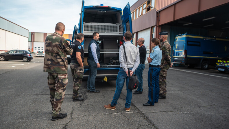 Derrière un véhicule de maintien de l'ordre, trois gendarmes en treillis, une gendarme en bleu et trois hommes en civil échangent