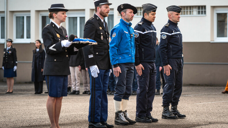 Quatre gendarme en rang prêts à recevoir une médaille. A leur droite une gendarme tient les médailles