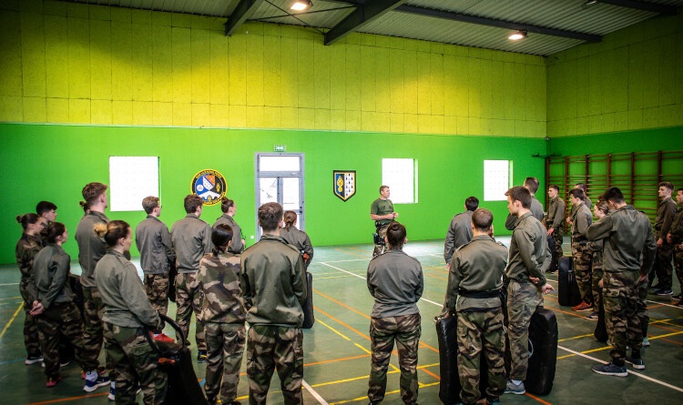Dans un gymnase aux tons verts, une vingtaine de jeunes en treillis baskets, réunis autour d'un instructeur qui explique le cours à venir de maîtrise sans armes de l'adversaire.