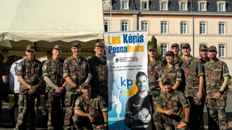 Une douzaine de jeunes élèves militaires en tenue, et souriant, posent devant un kakémono sur lequel est inscrit le nom de l'association Les Képis Pascalunes. Ils se tiennent à l'extérieur, devant un bâtiment.
