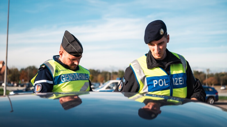Gendarme et policier allemand contrôlent un véhicule dont on ne voit que le toit.