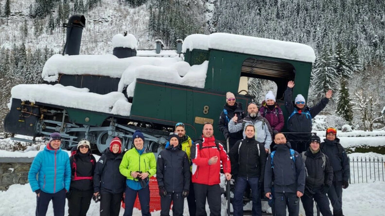 Quinze personnes chaudement vêtues posent, souriantes, devant une locomotive verte enneigée.