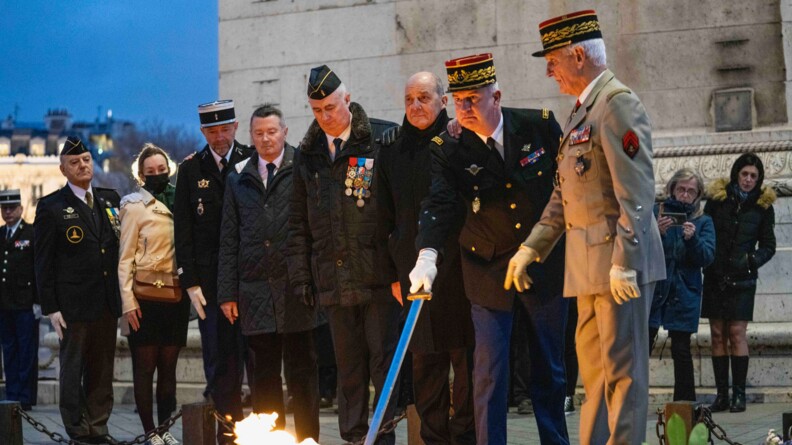 Un général de gendarmerie, muni de son sabre, et un général de l'armée de Terre, devant la flamme, entourés de plusieurs militaires et personnes en tenue civile.