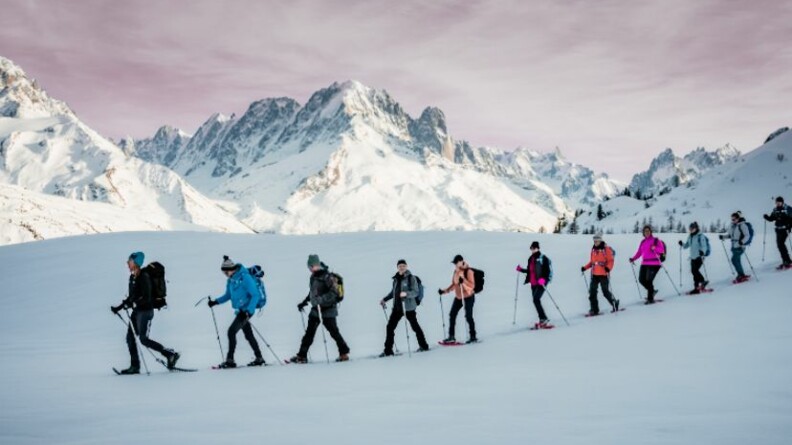 File de randonneurs en raquettes sur la neige avec les sommets enneigés en arrière plan.