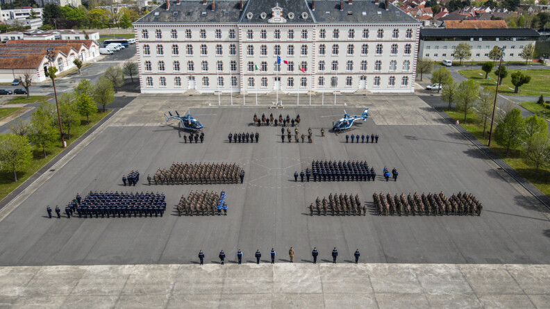Participants de l'exercice Midnight Express, en rang sur la place d'arme, avec deux hélicoptères de la gendarmerie avec en arrière-plan l'état-major