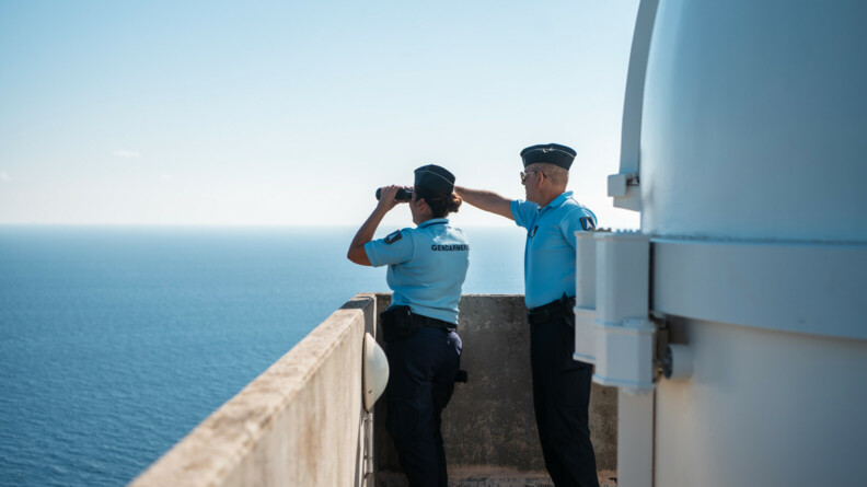 Deux gendarmes regardent au loin la mer à travers des jumelles.
