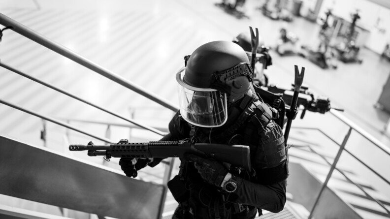 Photo en noir et blanc et en intérieur d'un militaire du PSPG en progression sur un escalier en métal.