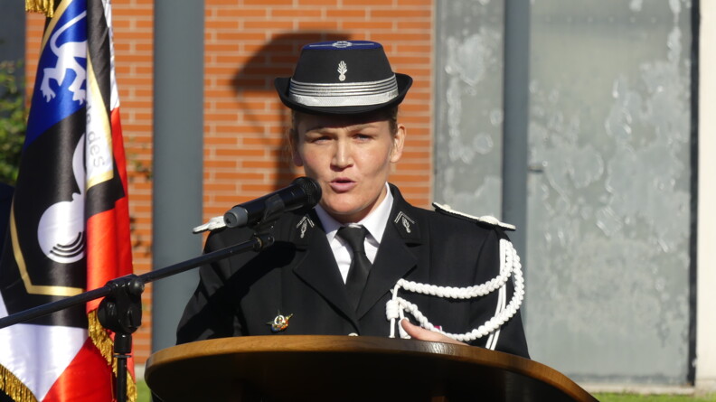 Une femme gendarme, commandant de compagnie, s'exprime au micro derrière un pupitre en bois