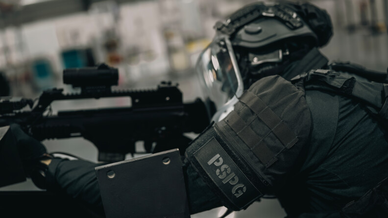 Image d'un gendarme, de profil. Sur son bras se trouve un brassard "PSPG" et il tient son arme.