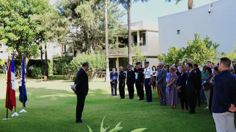 L'ambassadeur et ses personnels rassemblés devant les drapeaux pour observer une minute de silence suite au séisme.