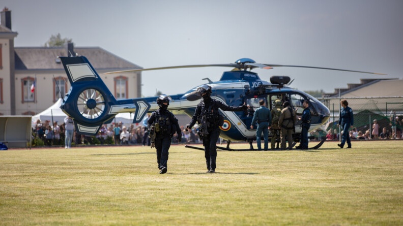 Un hélicoptère des forces aériennes au sol, sur un terrain du football, avec deux gendarmes des forces aériennes qui s'en éloignent.