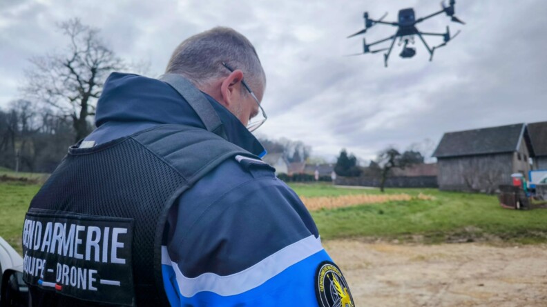 Un gendarme pilote de drone vu de dos avec le drone volant