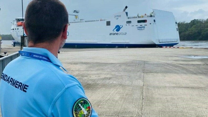Un gendarme de l'armement en polo bleu, regarde le bateau blanc d'Ariane Group, le canopée