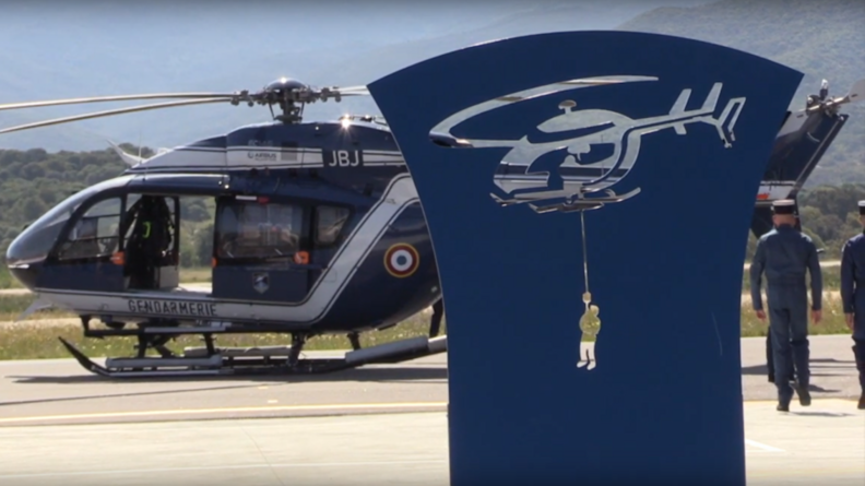 Hélicoptère de la Section aérienne de gendarmerie d'Ajaccio derrière une stèle représentant un sauvetage par hélitreuillage.