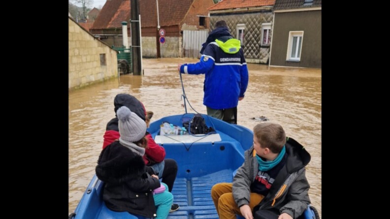 un gendarme tire une barque dans une zone inondée. Dans l'embarcation, se trouve deux enfants, un adulte et un petit chien.