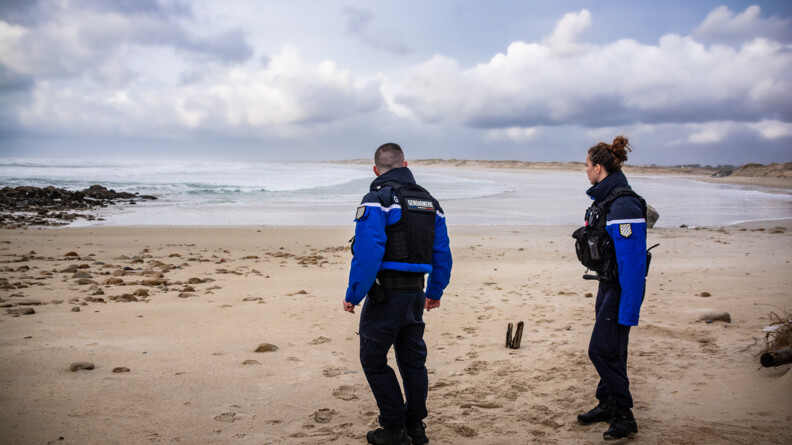 Deux gendarmes, un homme, à gauche, et une femme, à droite, arpentent une plage.