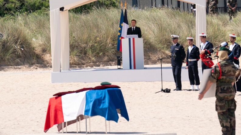 Le président de la république au fond prononce l'hommage de la nation à un pupitre bleu blanc rouge. Au premier plan, le cercueil de Léon Gautier, recouvert du drapeau français. Sur le côté de l'image un militaire en tenue de commando et des marins de la Marine nationale.