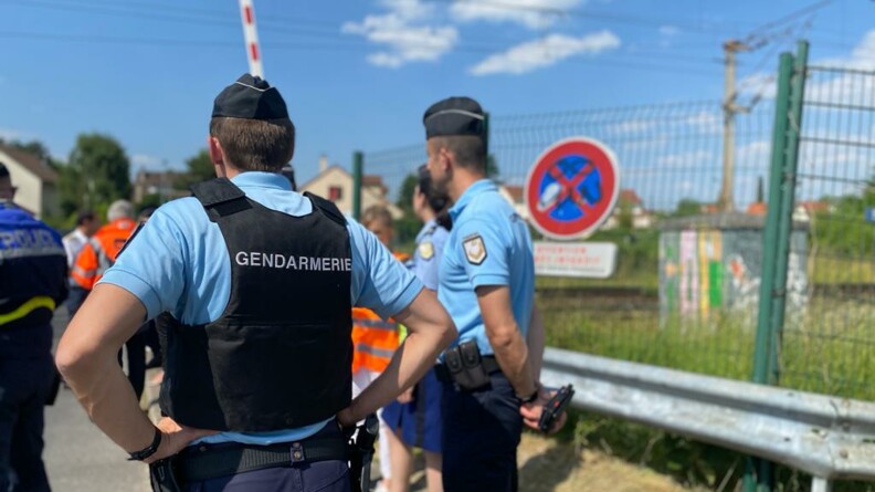 Au premier plan, un gendarme vu de dos et un autre de profil ; au second plan, un policier à gauche et des agents SNCF, à proximité d'un passage à niveau.