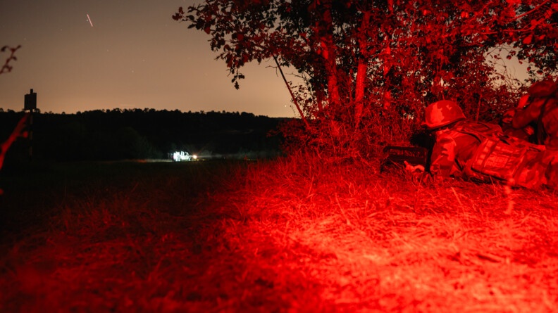 Militaires postés de nuit surveillant un véhicule.