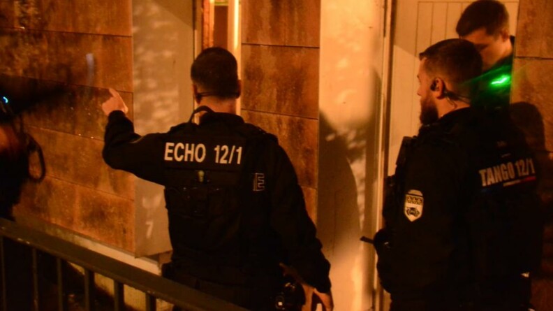 Trois gendarmes mobiles, dans la pénombre, devant les entrées d'un bâtiment.