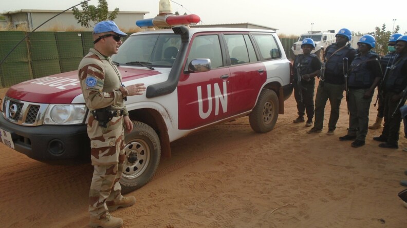 Un gendarme en mission ONU au Mali avec un véhicule de l'ONU et des policiers maliens.
