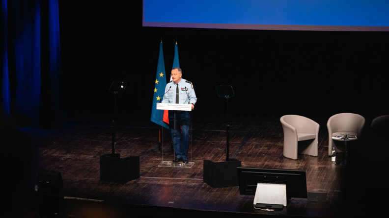 Le directeur général de la gendarmerie, sur une scène, derrière un pupitre. Derrière lui, le drapeau français et le drapeau européen.