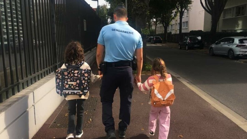 Un gendarme dans la rue amenant ses deux enfants à l'école.