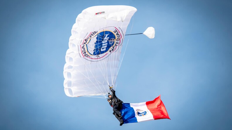 Une parachutiste en plein vol avec un grand drapeau français accroché à sa jambe