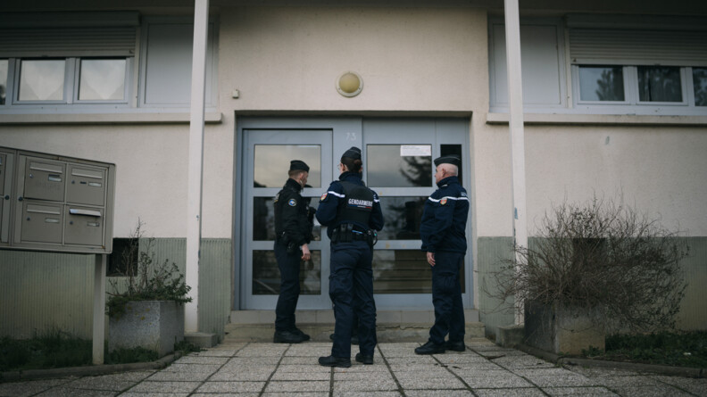 Trois gendarmes de dos devant une porte d'immeuble.