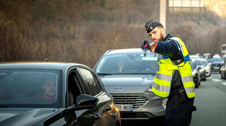 Un gendarme avec une chasuble jaune conseille un automobiliste sur la route.