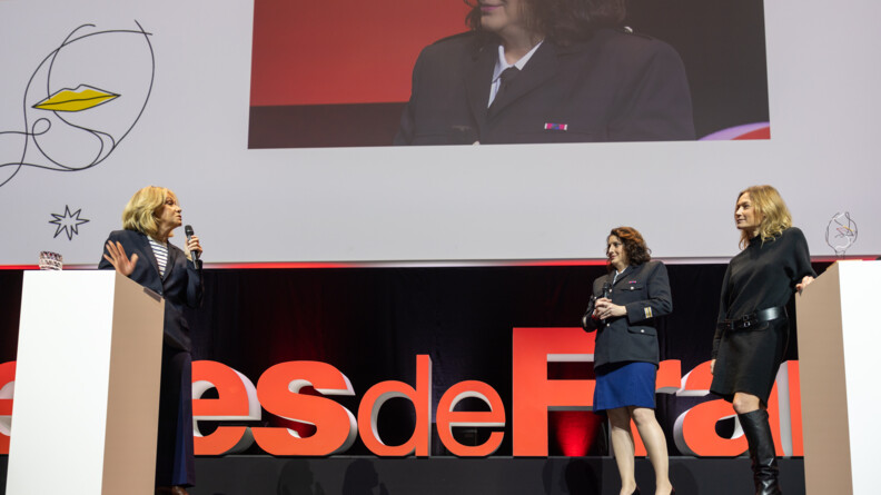 Le lieutenant-colonel Marie-Laure Brunel-Dupin à droite de la scène de la remise du prix, entourée de part et d'autre de deux femmes; en fond de scène un zoom sur son portrait