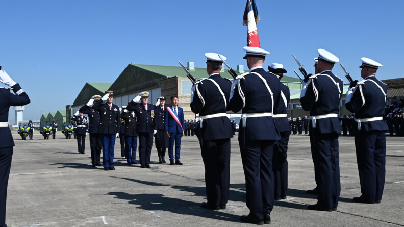 Sur une piste d'aéroport, devant un hangar, se déroule la cérémonie des 80 ans. La formation du porte drapeau se fait saluer par le commandement.
