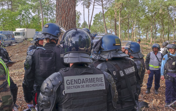 Un enquêteur de la section de recherches de Versailles, vu de dos, en tenue de maintien de l'ordre, aux côtés de plusieurs gendarmes mobiles, également vus de dos, lors d'un stage à Saint-Astier. La scène se passe dans les bois.