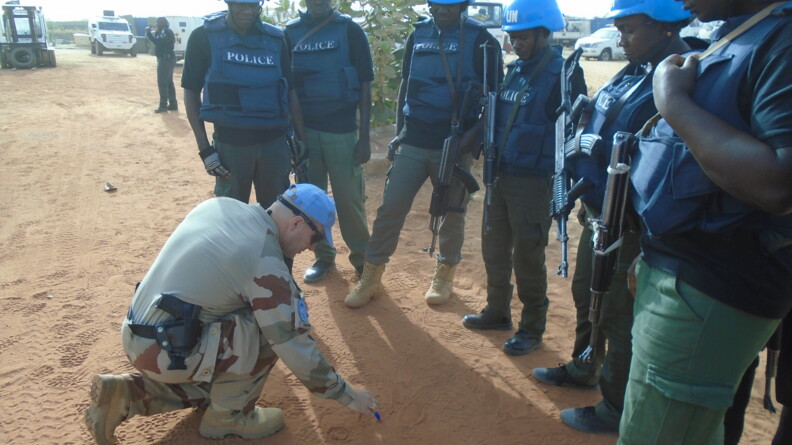 Un gendarme dessine un croquis dans le sable pour expliquer une manoeuvre aux militaires de l'unité.
