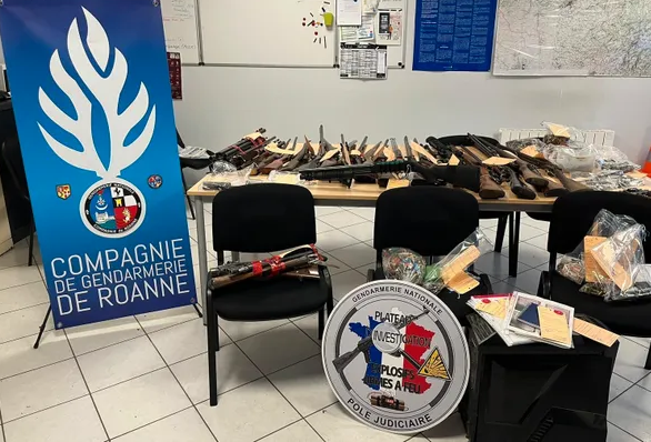 Des saisies d'armes et de munitions sous scellés sur une table, à gauche le kakémono de la compagnie de gendarmerie de Roanne, au centre la rondache du Plateau d'investigation explosifs armes à feu