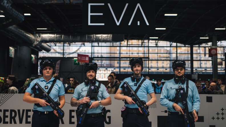 Dans un grabd hall d'exposition, quatre gendarmes gamers posent en tenue de gendarme, armés d'une arme de jeu. Tpus portent une casquette noire portant le sigle EVA.