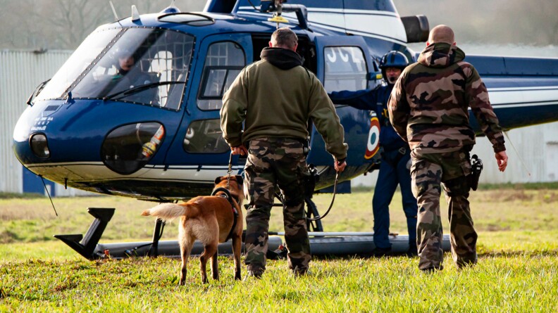 Un malinois tenu pardeux gendarmes se dirigent vers un hélicoptère gendarmerie où les attend un gendarme pilote