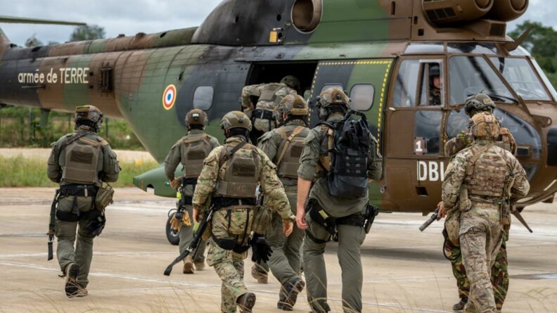 Groupe de militaires en treillis kaki vus de dos, se dirigeant vers un hélicoptère du GIH.