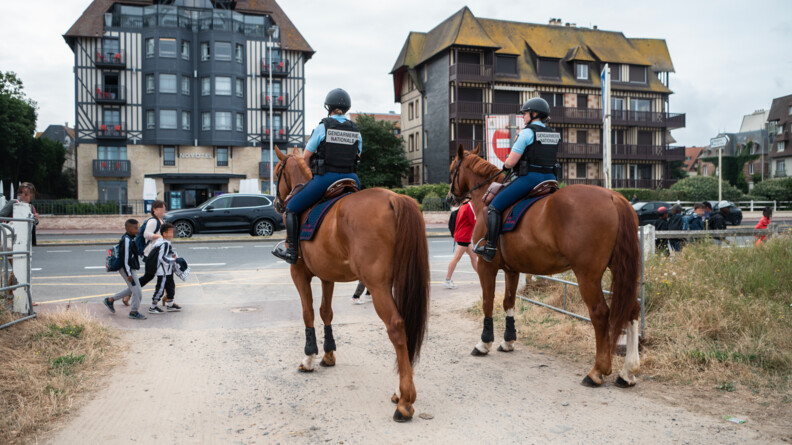 Deux gendarmes à cheval du de dos, pendant que des enfants en tenue de sport traversent devant eux sur le trottoir