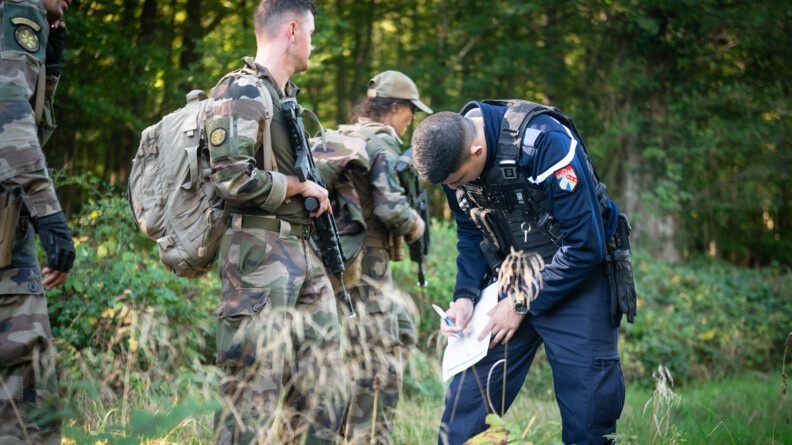 A la lisière d'une forêt, un gendarme remplit une fiche en prenant appui sur sa cuisse, face à trois militaires de l'armée de Terre