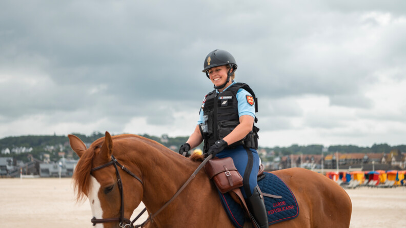 Une gendarme sur son cheval, sur la place, de trois quart face, le sourire aux lèvres