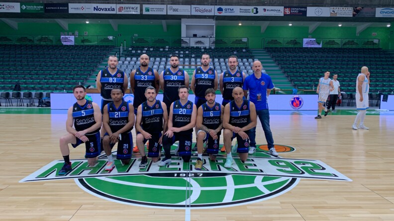 Les onze joueurs et l'entraîneur du Club sportif et de loisirs de la gendarmerie (CSLG) d’Antibes Juan-les-Pins posent au centre du terrain de basket de la salle de Nanterre.
